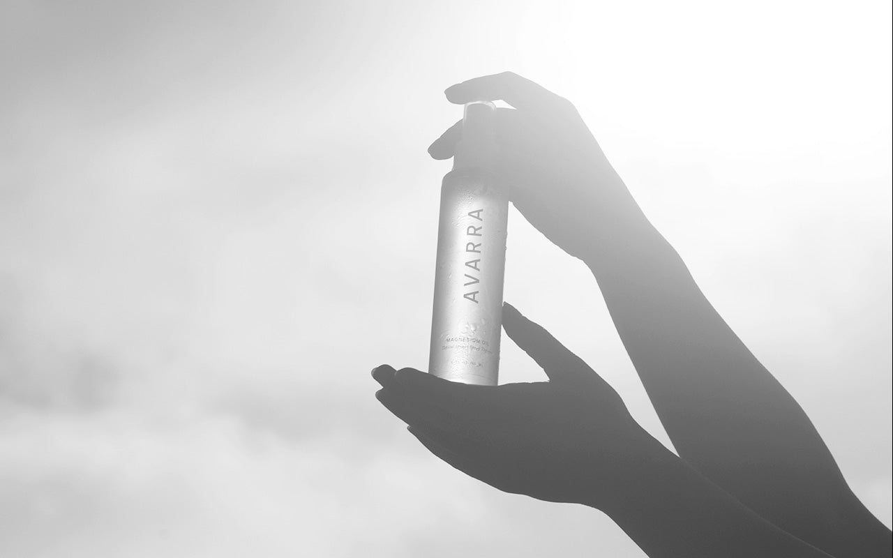 Silhouette of hands holding Avarra 150ml magnesium oil spray bottle up to the sun