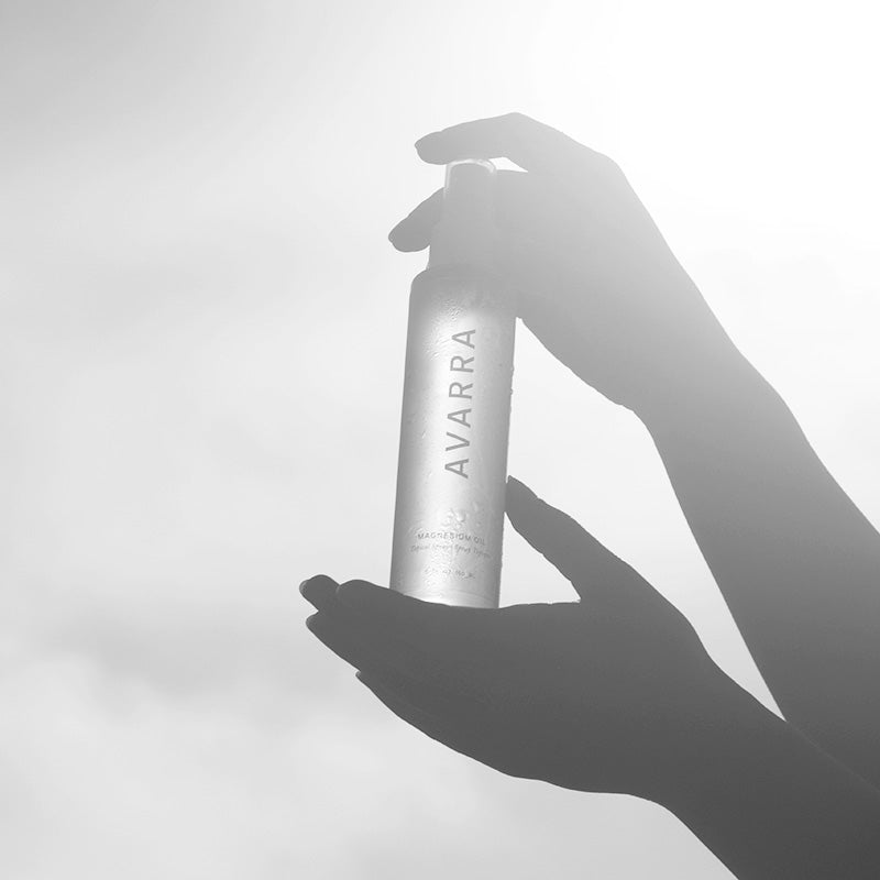 Silhouette of hands holding Avarra 150ml magnesium oil spray bottle up to the sun